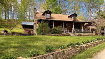 A log cabin with a stone chimney, a porch, and a stone retaining wall.