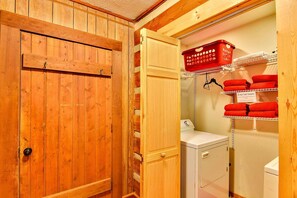 A laundry room with wooden cabinets, a washing machine, and a shelf with red towels. - Rustic Log Cabin Rental with a Hot Tub near Asheville, North Carolina (Clyde)