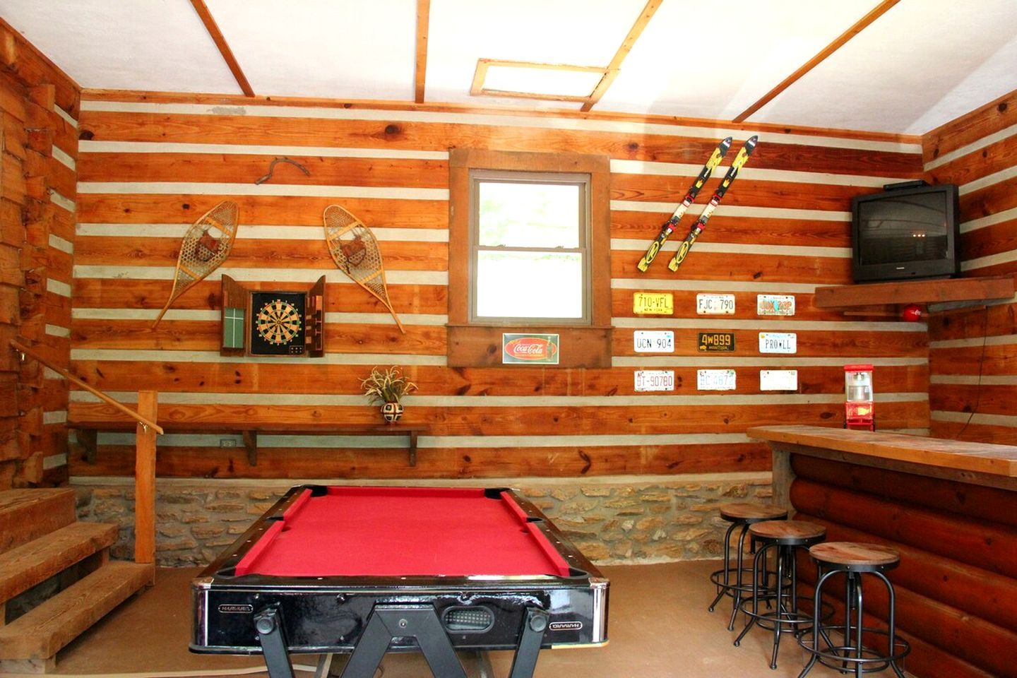 Interno di una baita in legno con tavolo da biliardo, freccette, televisore e targhe appese al muro.