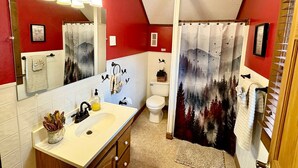A bathroom with a white sink, a mirror, a toilet, and a shower curtain with a forest design. - Rustic Log Cabin Rental with a Hot Tub near Asheville, North Carolina (Clyde)