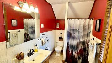 A bathroom with a white sink, a mirror, a toilet, and a shower curtain with a forest design.