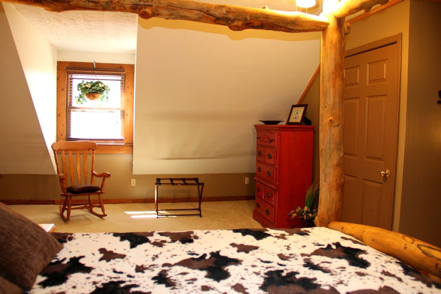 A bedroom with a sloped ceiling, a rocking chair, a dresser, and a door.