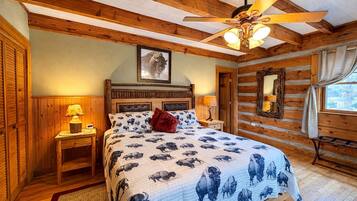 Une chambre avec un plafond en bois, un lit recouvert d’une courtepointe à motifs de buffle, une tête de lit, des lampes de chevet et un ventilateur de plafond.