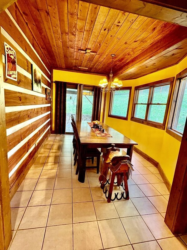 Un intérieur en bois avec une table et des chaises, un lustre et de grandes fenêtres.