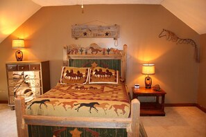 Une chambre à coucher avec un lit agrémenté de linge de lit sur le thème des chevaux, une tête de lit en bois ornée de sculptures d’animaux et deux lampes de chevet.
