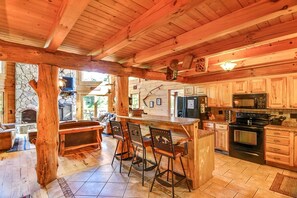 A wooden cabin interior with a stone fireplace, a kitchen with wooden cabinets, and a bar area with stools. - Luxury Vacation Rental with a Hot Tub for Rent in Clyde, North Carolina (Clyde)