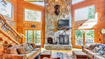 A log cabin interior with a stone fireplace, leather sofas, and a television.