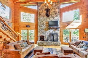 A log cabin interior with a stone fireplace, leather sofas, and a television.