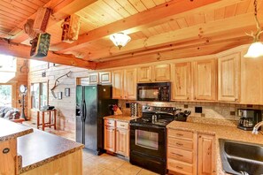Interior de una cabaña de madera con cocina, que incluye un refrigerador, estufa, microondas y alacenas de madera.