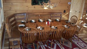 A wooden dining room with a large table and chairs, a chandelier, and a wall-mounted painting.