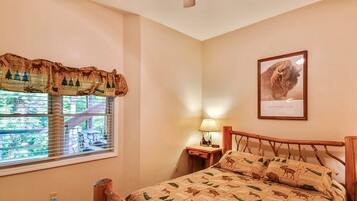 A bedroom with a bed, a nightstand, a lamp, a window with a view, and a framed picture on the wall.