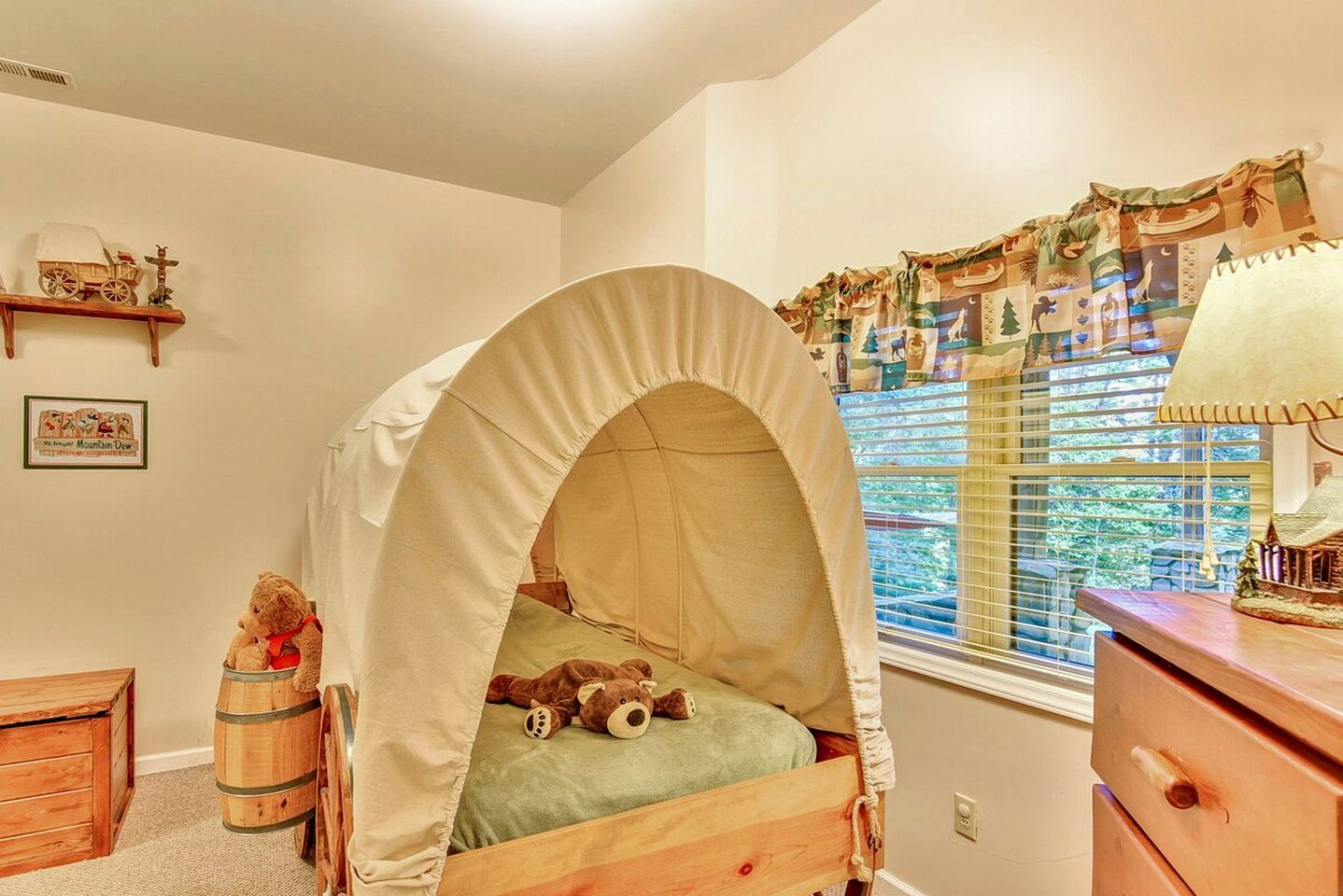 A child's bedroom with a canopy bed, a wooden dresser, a small wooden chest, and a window with curtains.