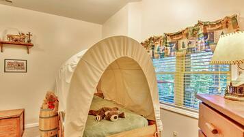 A child's bedroom with a canopy bed, a wooden dresser, a small wooden chest, and a window with curtains.