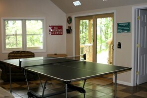 A ping pong table in a room with a 'No Smoking Allowed' sign, a 'Pool Room Rules' sign, and a view of the outdoors through a door. - Luxury Vacation Rental with a Hot Tub for Rent in Clyde, North Carolina (Clyde)