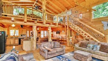 Ein geräumiges Blockhaus-Interieur mit hohen Decken, Holzbalken, einer Treppe und einer gemütlichen Sitzecke.