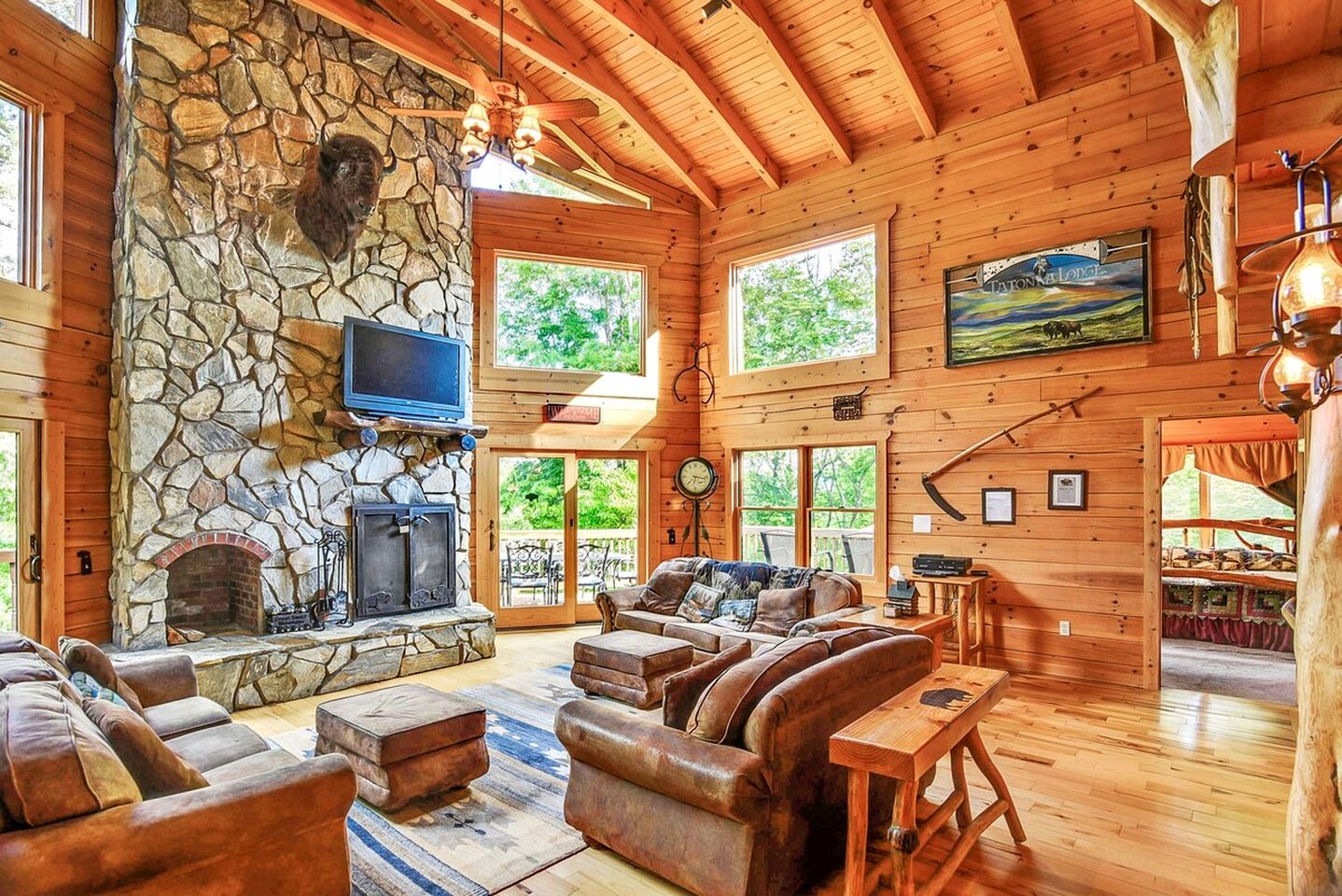 A log cabin interior with a stone fireplace, leather furniture, and a television mounted above it.