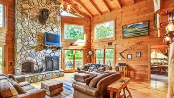 A log cabin interior with a stone fireplace, leather furniture, and a television mounted above it.