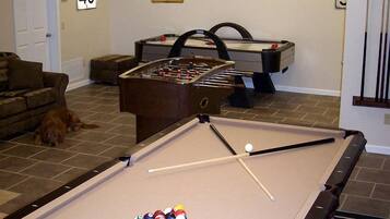 A pool table with balls, a foosball table, a dog, and a speed limit sign.