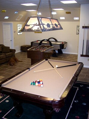 A pool table with balls, a foosball table, a dog, and a speed limit sign.