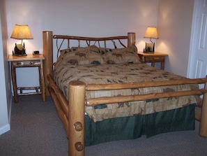 A wooden bed with a patterned bedspread, two bedside tables with lamps, and a carpeted floor. - Luxury Vacation Rental with a Hot Tub for Rent in Clyde, North Carolina (Clyde)