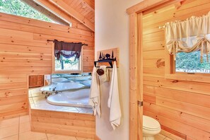 Baño de cabaña de madera con una bañera grande, un inodoro y una ventana con cortinas.