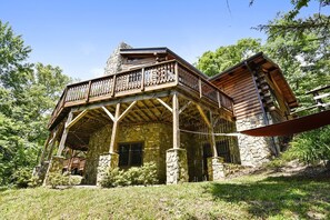 A rustic cabin with a stone exterior, wooden balcony, and a chimney. - Luxury Vacation Rental with a Hot Tub for Rent in Clyde, North Carolina (Clyde)