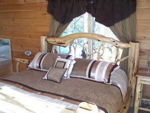 Una habitación de cabaña de madera con una cama, un reloj en una mesita de noche y una ventana con cortinas.