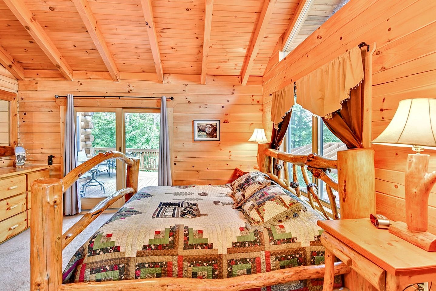 A wooden cabin bedroom with a bed, a nightstand, a lamp, and a window with curtains.