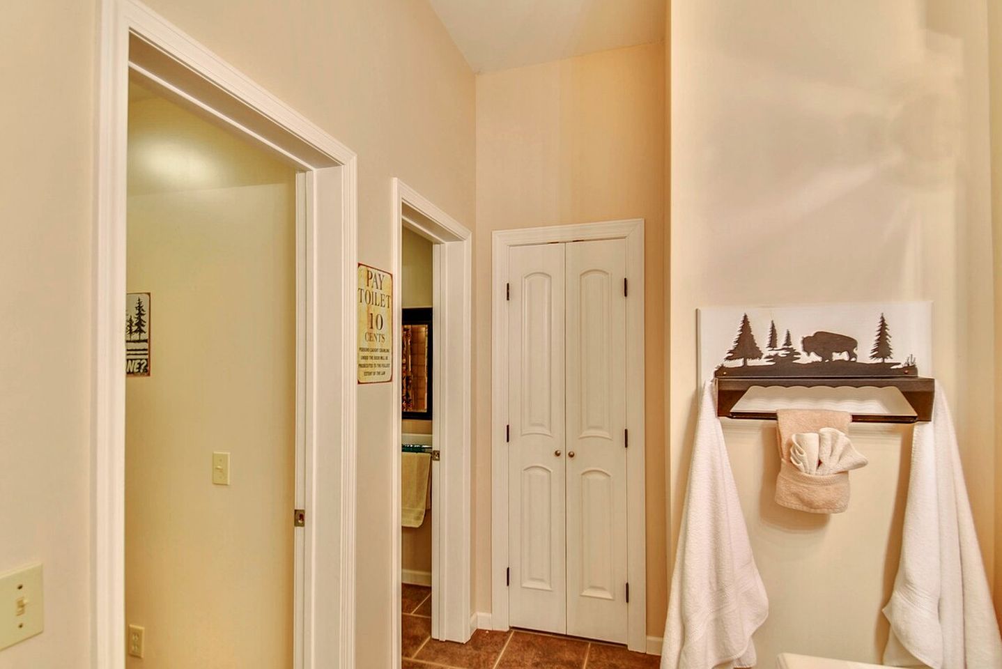 A hallway with a white door, a sign indicating a toilet and a 10 cents fee, and a towel rack with a towel.