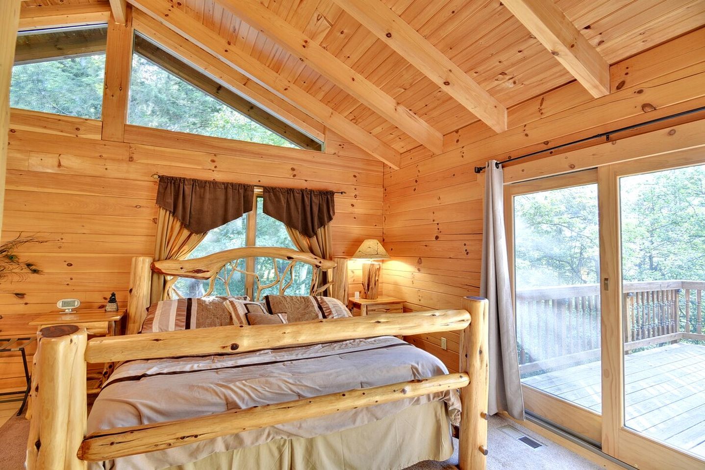 A wooden cabin bedroom with a bed, windows, and a view of the outdoors.