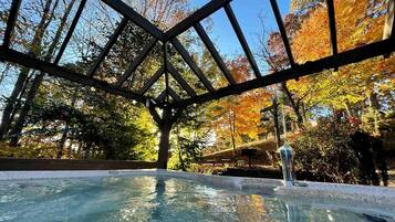 A hot tub under a wooden pergola with a view of autumn trees.