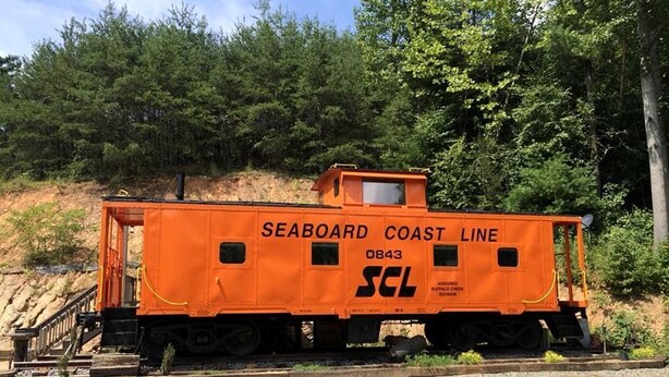 Een rangeerwagon van Seaboard Coast Line met nummer 0843, op een spoor met een gazon en bomen op de achtergrond.