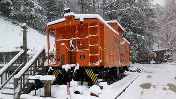 A stationary train caboose in a snowy setting with a wooden staircase leading up to it.