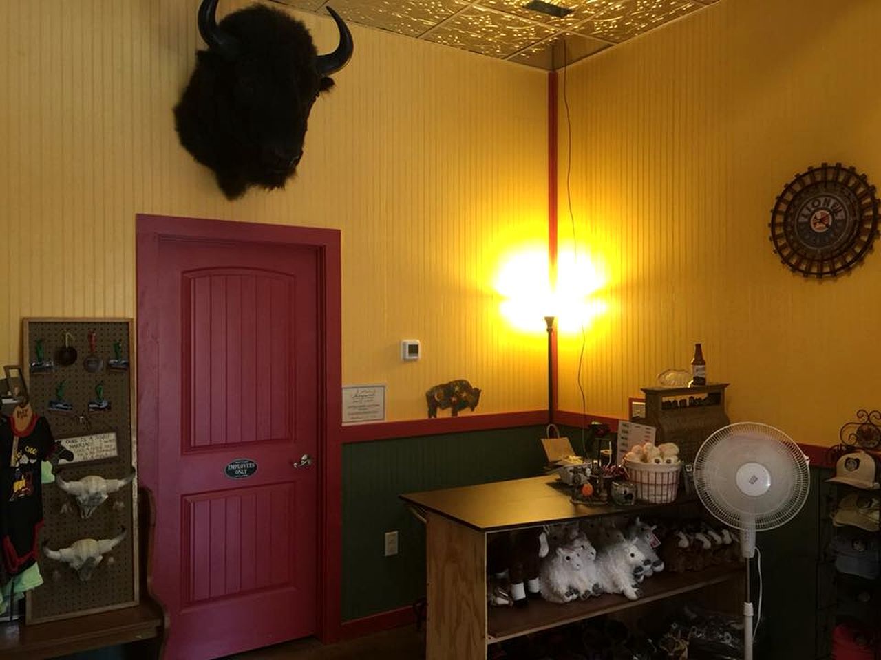 Una stanza con una porta rossa, una lampada a muro, una ventola e uno scaffale con peluche.