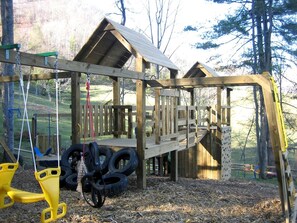 Une structure de jeu en bois avec des balançoires classiques et des balançoires en forme de pneu.
