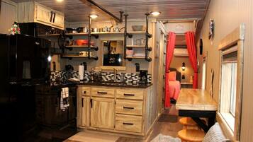 A compact kitchen with wooden cabinets, a black refrigerator, and a dining area with a bench and table.