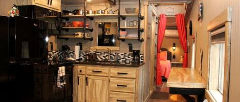 Una cocina compacta con armarios de madera, un refrigerador negro y una zona de comedor con banco y mesa.