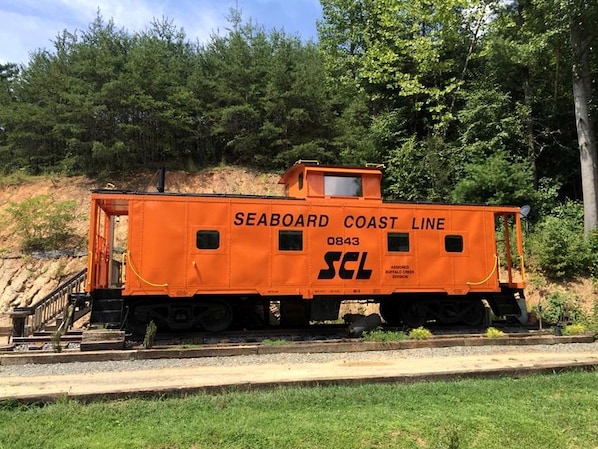 A Seaboard Coast Line train caboose with the number 0843, located on a track with a grassy area and trees in the background.