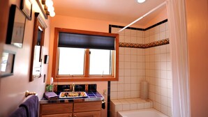 A bathroom with a window, a bathtub, a vanity with a mirror, and a shower area.