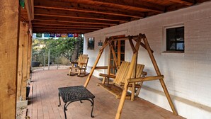 A covered patio with a swing set, two rocking chairs, and a metal table. - Spacious Cabin Rental with Beautiful Mountain Views near Pinos Altos, New Mexico (Silver City)