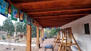 A covered outdoor area with a swing set, a bench, and a building with a window.