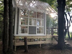 A wooden cabin with multiple windows, a deck, and a thatched roof.