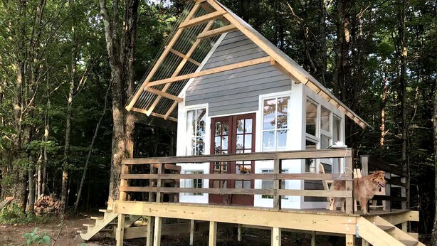 Une terrasse en bois menant à un chalet doté d’un toit à deux versants et de grandes fenêtres.