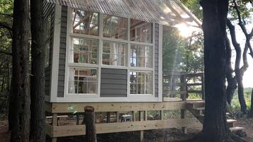 A wooden cabin with multiple windows, a deck, and a thatched roof.