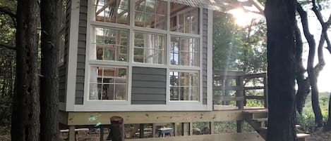 A wooden cabin with multiple windows, a deck, and a thatched roof.