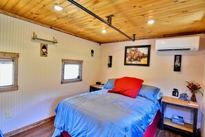 A bedroom with a bed, a nightstand, a window, an air conditioning unit, and a wall-mounted light fixture.