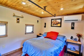 A bedroom with a bed, a nightstand, a window, an air conditioning unit, and a wall-mounted light fixture.
