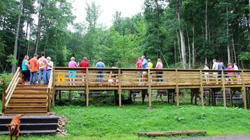 A wooden bridge with people standing on it, surrounded by a forested area.