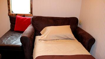 A single bed with a brown headboard and a red pillow, a window with a wooden frame, and a wall with vertical lines.