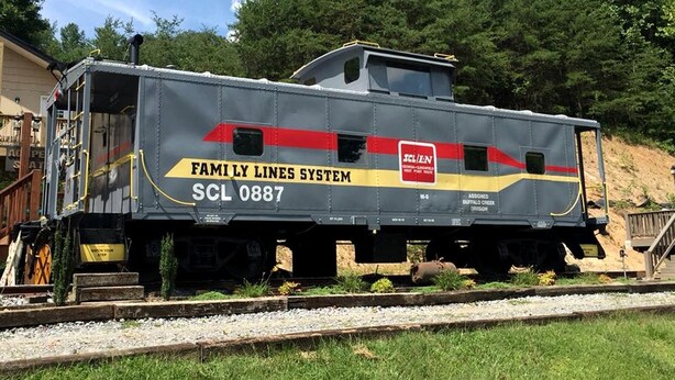 A train car with 'Family Lines System' and 'SCL 0887' visible, parked on tracks with a forested background.